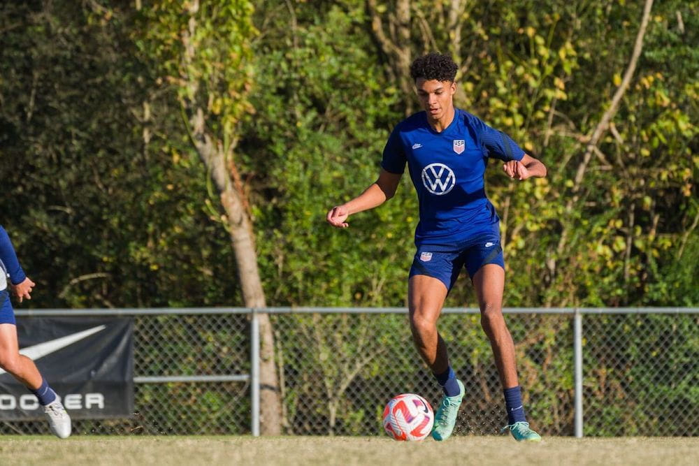 A man in a blue uniform dribbles a soccer ball on a field
